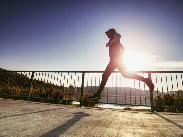 Tall slim man run on the lake terrace against the backdrop of a beautiful sunrise. Shore of mountain lake with dark forest hills