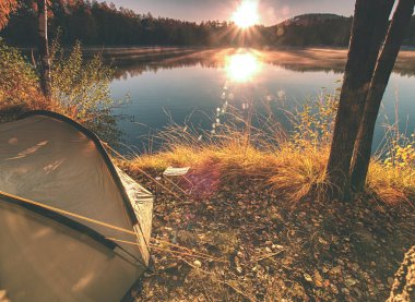 Yeşil kamp çadır erken sabah göl kıyısında. Şafak güneş touch forest hill karşı