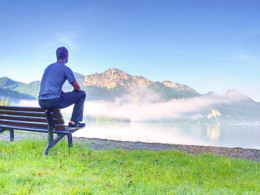Adam yalnız park sonraki gölde bir bankta otur. Dağ silsilesi düzgün göl yüzeyi üzerinde muhteşem manzaralı.