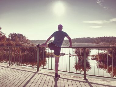 Sabah egzersiz çalıştırmadan önce bacaklarını esnetiyor uzun boylu sporcu kasları kadar ısınma. Dışarıda güneşli sabah dağ Gölü