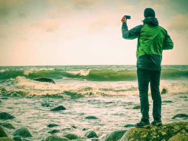Akıllı telefon kullanarak sahil günü Man fotoğrafları. Turist akşam deniz fotoğraf çeker. 