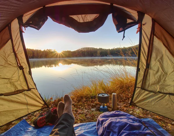 View over man body in camping tent to lake in beautiful morning. Enjoy freedom in pure nature.