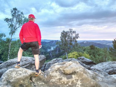 Kırmızı bere, Kırmızı jumper ve pantolon içinde hiking ile uzun boylu adam akşam düşmek. Keskin kumtaşı dağ uçurum kenarı