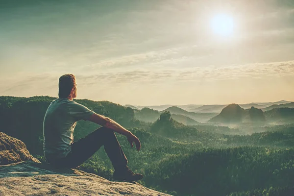渓谷の夕日を見ながら丘の上に岩の上に座っている男性ハイカーの背面図 — ストック写真