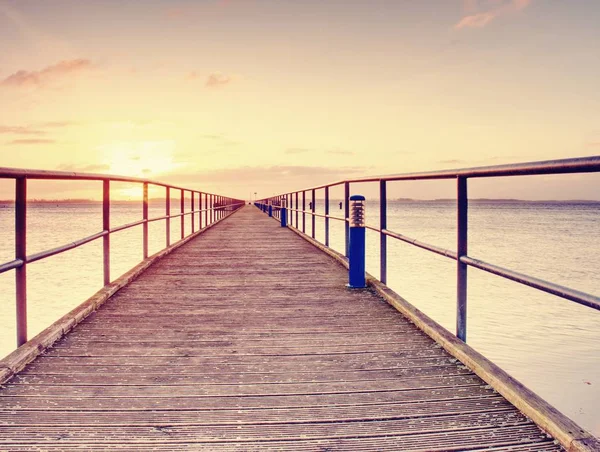 Daybreak morning wooden dock (pier) orange sea and clear sky background. View of wooden pier or dock in sea.