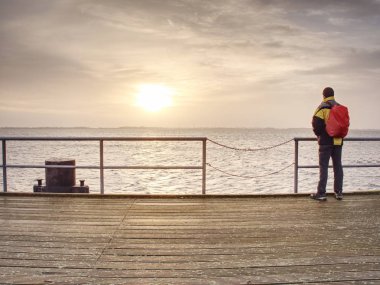 Yalnız adam iskele ve Küpeşte suya üzerinden bakmak. Güneşli açık mavi gökyüzü yumuşak su seviyesi. 