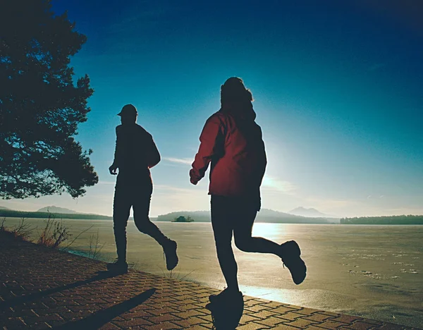 Deportes pareja loco saltar en el camino del parque alrededor de lago congelado — Foto de Stock