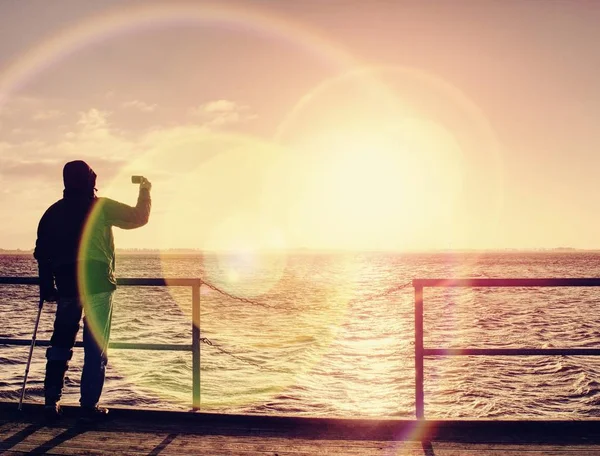 Mann mit Handy in der Hand fotografiert Sonnenaufgang auf Fährhafen-Maulwurf — Stockfoto