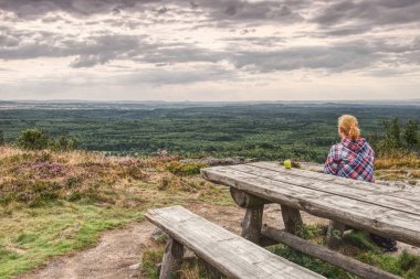 Sarışın kız yalnız yukarıda uçurum kenarında oturur. 