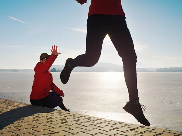 Girl and boy running while sun makes reflections in frozen lake surface. Regular sports activities do partners together