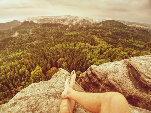 Young man sit down on mountain edge barefoot.