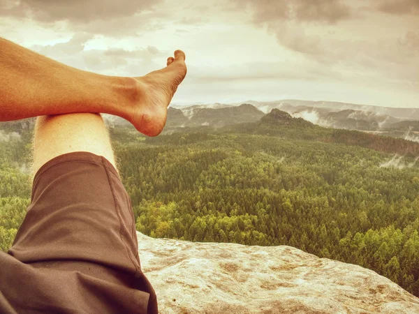 Young man sit down on mountain edge barefoot.
