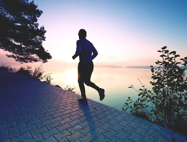 Hombre corriendo sobre el pavimento de la orilla del lago al amanecer o al atardecer —  Fotos de Stock