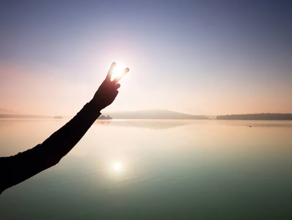 Man hand makes shadow symbols  to Sun. Misty daybreak at lake. — Stock Photo, Image
