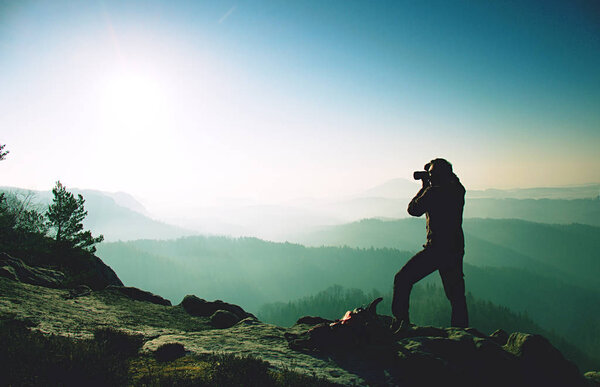 Photographer stay at tripod on summit. Man photographer during hike