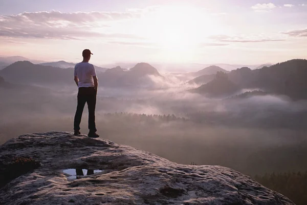 スポーティなスーツを着たハイカーは、岩の頂上に立ち、霧を見守る — ストック写真