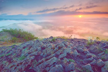 Sisli vadiye manzaralı kayalık dağın tepesinde gündoğumu.