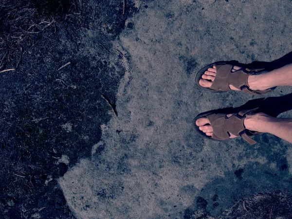 Male hairy legs with sandals rest on rocky summit above valley