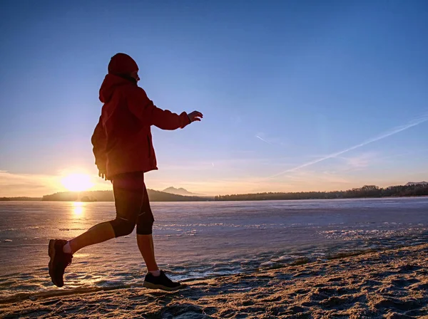 Mujer corriendo a lo largo de la orilla de un lago congelado en invierno primavera — Foto de Stock