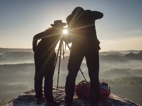 Two hikers taking pictures and talk on top of mountain. Two photographers