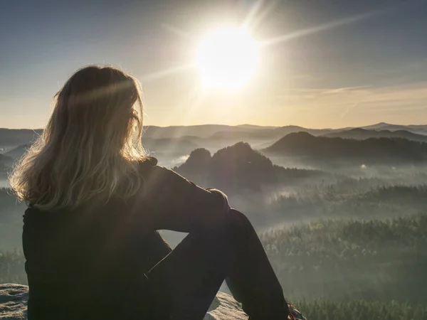 Blonde vrouw zittend op de rand van de berg klif tegen surise — Stockfoto