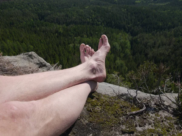 Tired hikers legs without shoes. Man hiker legs climbed at mountain peak rock