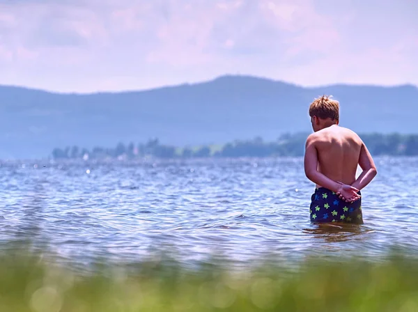 Niño en pantalones cortos de natación azul permanecer en el agua fría del lago —  Fotos de Stock