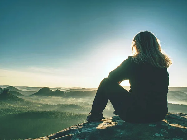 Blond woman sitting on edge of the mountain cliff against surise — Stock Photo, Image