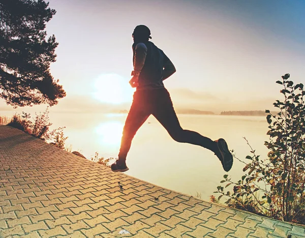 Silhouette of runner man along on the beach at sunset with sun