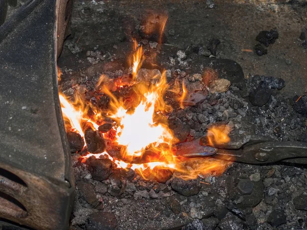 Forge with strong flames. Pliers hold horse shoe — Stock Photo, Image