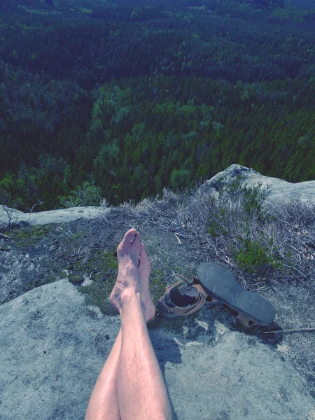 Male hairy legs with sandals rest on rocky summit above valley