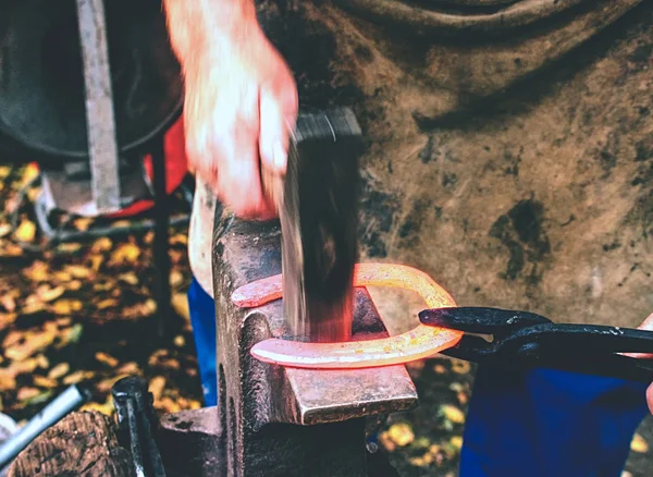 Blacksmith arms forge horseshoe with hammer on anvil