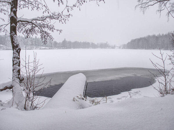 Winter lake shore with opened water in ice under channel tube