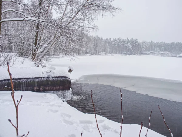 Orilla del lago de invierno con agua abierta en hielo bajo el tubo del canal — Foto de Stock