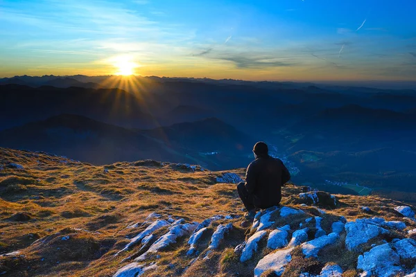 Muž sedí na popraskaném vrcholu v Alpách a dívá se na úžasný západ slunce — Stock fotografie