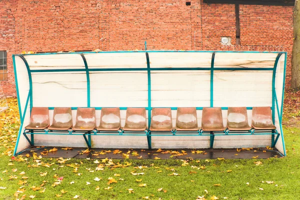 Old worn bench for reserve football players, old and ruined. Autumn morning with fallen leaves