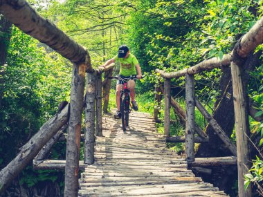 MTB 'deki çocuk akarsu üzerindeki ahşap köprüden geçiyor. Çocuk tırabzanı tut ve suyun haykırışını izle. 24 Mayıs 2018, Prag 'da park
