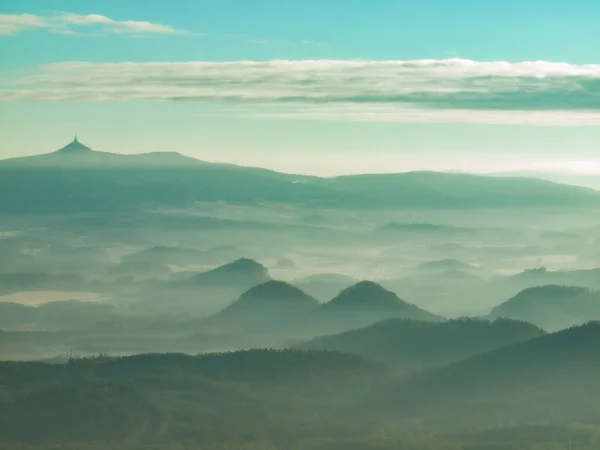 Blue green mist cover landscape. The sun shines against the white mist floating above forest.