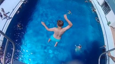  Çocuk açık havuz kompleksindeki mavi su yüzme havuzuna atlıyor. Dikiz aynası. Yavaş çekim