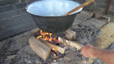 Yaşlı adam ateşe odun ekliyor. Bahçe mutfağında yemek pişirmek, kazana soğan eklemek ve tahta kaşıkla dönmek. Yavaş çekim..