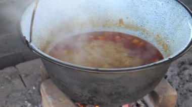 Kabaran ev yapımı güveci olan bir karnabaharın dairesel manzarası. Kazanda yanan kamp ateşinde Gulaş çorbası pişirmek. Yavaş çekim.