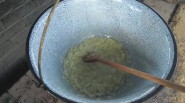 Soğan ve tereyağı pişirip, doğal ateşin üzerinde tahta kaşıkla pişirmek. Bahçe mutfağında yemek pişirmek..