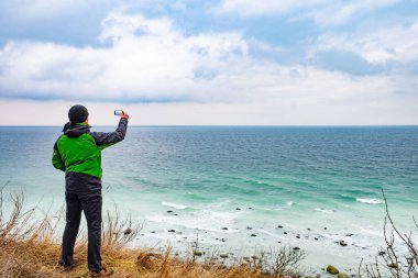 Telefon kameralı gezgin sahildeki rüzgarlı denizin fotoğrafını çekiyor..