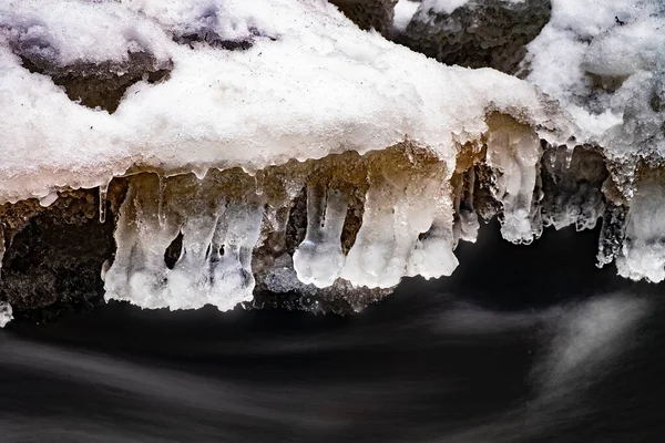 溪流上方结冰的冬季冰柱 有泡沫和雪花的冰冻水 — 图库照片