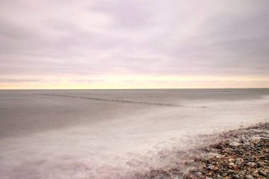 Gün batımında okyanusun üzerinde uzun süre bulutlar görülür. Ahşap bir dalgakıran hattı.