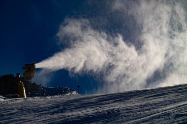Kayakçılar ve snowboardcular körüklü kar tabancası kullanıyorlar. İtalya kayak merkezinde yoğun kar bulutu yamaçta yüzüyor..