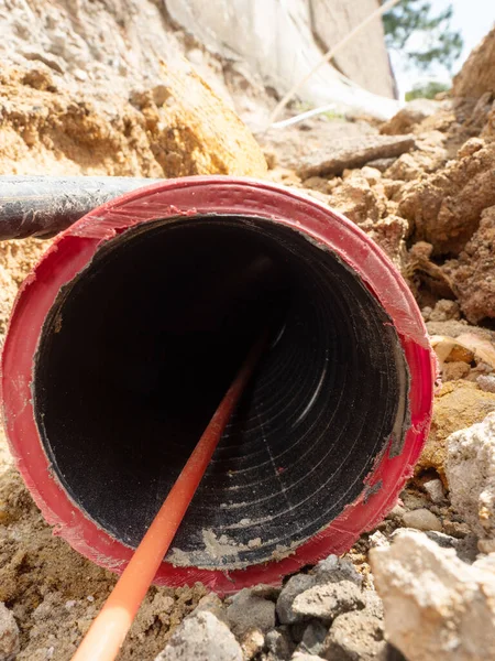 Detail of optic fiber wire in ribbed flexible red plastic tube, thin trench at lamp post