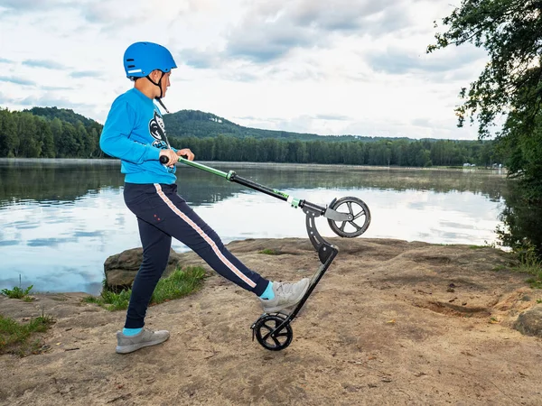 スクーターの男の子は公園の背景に岩の湖の銀行でトリックを行います — ストック写真