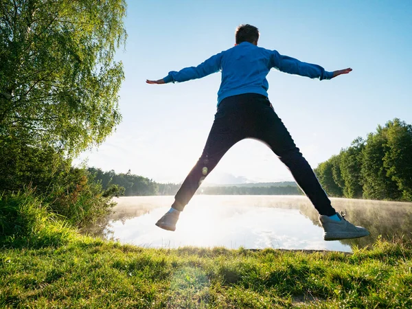 Funny Boy Jumping Outdoor Lake Gainst Sunset 青いトレーナーと白いスニーカーの青年 — ストック写真