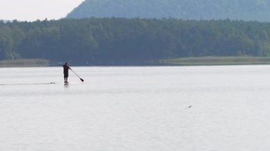 Gün batımında Machovo Gölü 'nde yüzen bir adam. Standup paddle tahtası, çarpıcı hava ve huzurlu su seviyesi ile popüler spor.